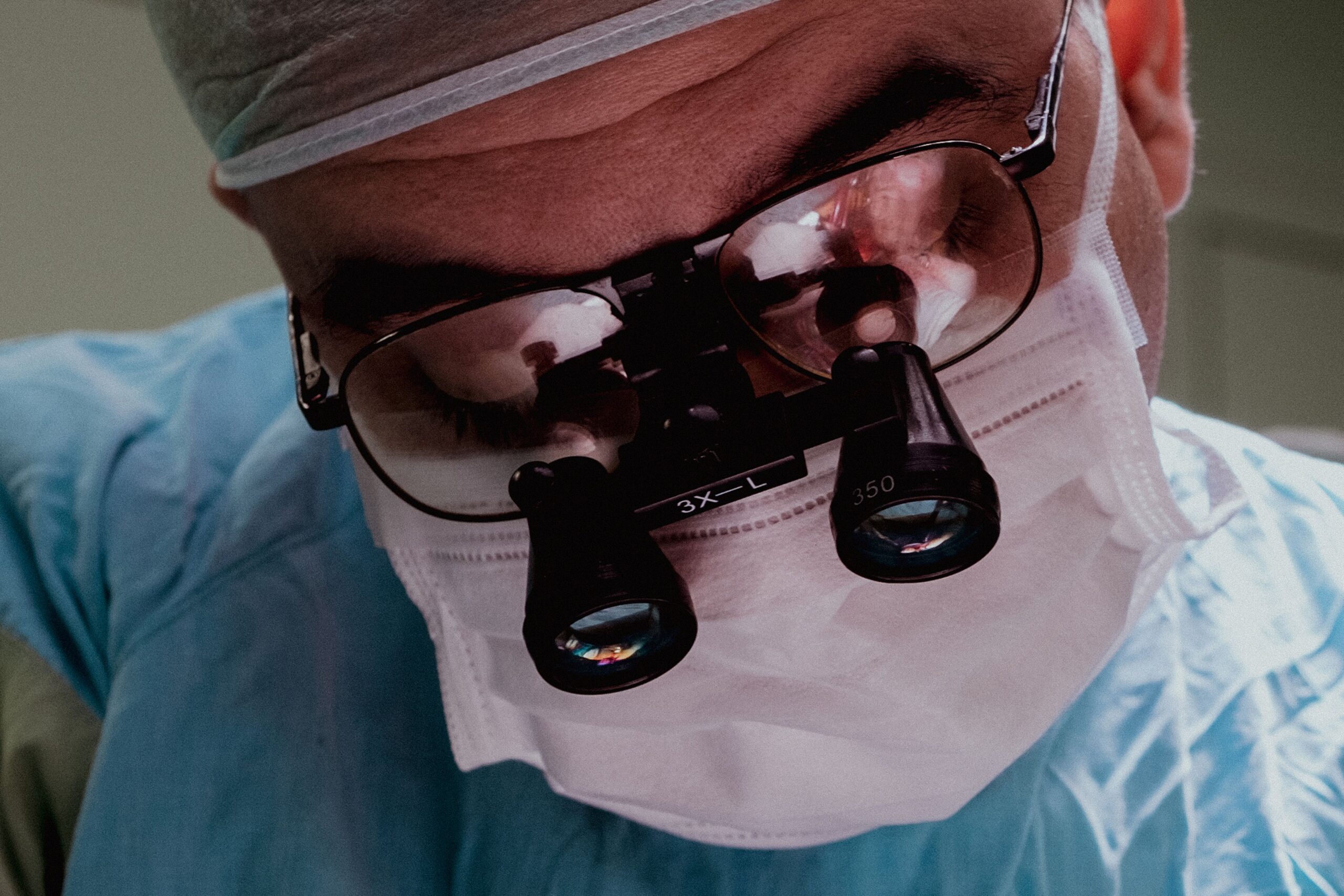 Close-up of a surgeon wearing surgical mask and loupes, demonstrating focus and expertise in medical procedure.